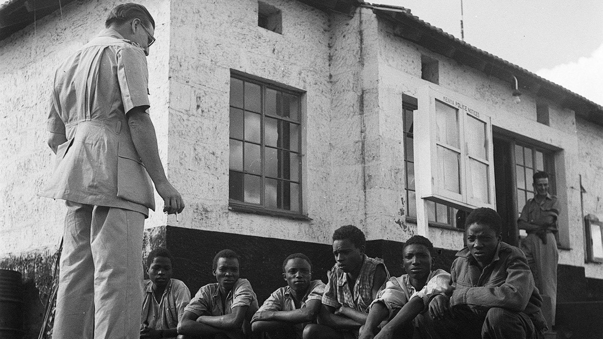 Kikuyu tribesmen suspected of belonging to the Mau-Mau movement are interrogated by a police inspector. 1952. 